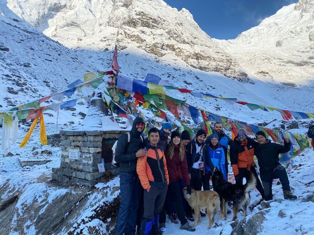WeRoad-Reisegruppe posiert lächelnd vor einem Gebetsfahnen-Denkmal in einer verschneiten Himalaya-Landschaft