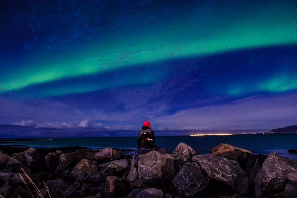 Reisender beobachtet grüne Nordlichter (Aurora Borealis) über dem Meer in Island