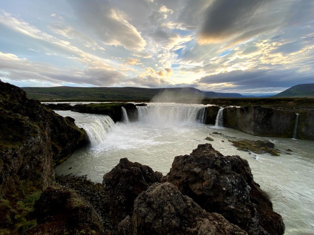 Malerischer Goðafoss Wasserfall unter dramatischem Sonnenuntergangshimmel.