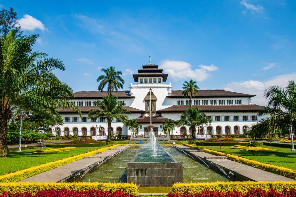 Historisches Gedung Sate Kolonialgebäude in Bandung, West-Java, mit Brunnen und Palmen im Vordergrund.