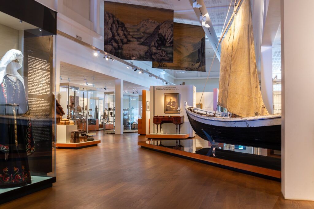 Ausstellung im Nationalmuseum Island mit traditioneller Kleidung, Segelboot und historischen Artefakten.