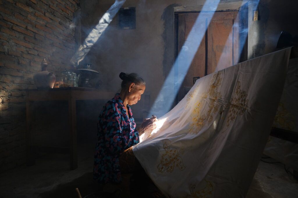 Ältere Frau trägt in einer traditionellen Werkstatt flüssiges Wachs auf ein Batik-Tuch in Yogyakarta auf.