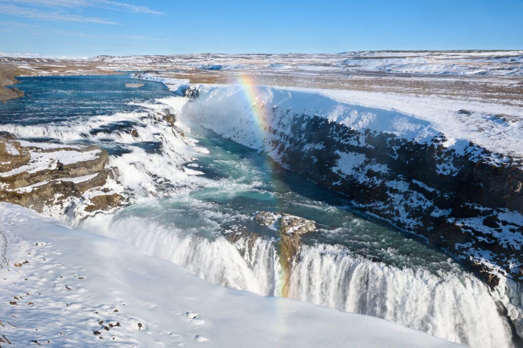 Winteransicht des Wasserfalls Gullfoss mit Schnee und Regenbogen in der Gischt.