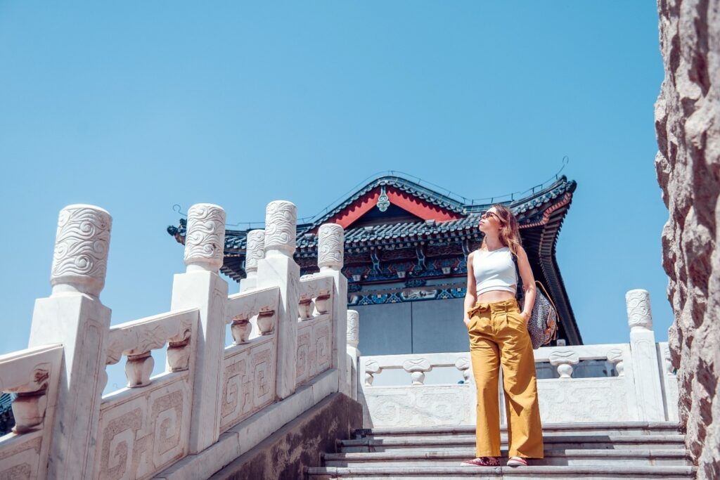 Tourist standing on stone steps in front of a traditional Chinese gate.