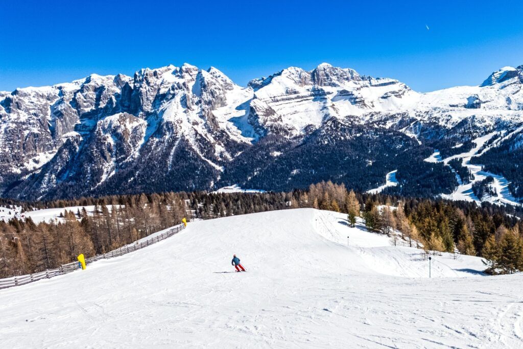 Skifahrer auf sonniger Piste in den Dolomiten vor schneebedeckten Berggipfeln.
