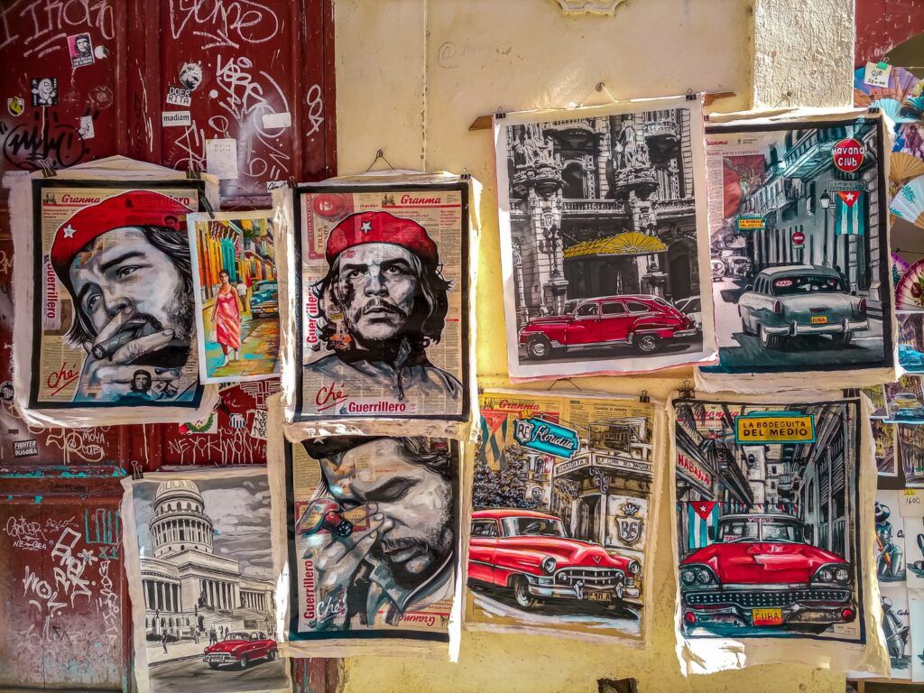 Carteles artísticos que representan al Che Guevara y coches clásicos cubanos en una pared de La Habana.