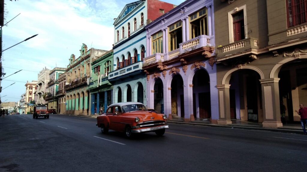 Un coche naranja clásico en una calle llena de coloridos edificios coloniales en La Habana.
