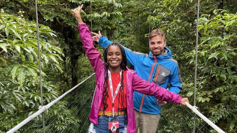 Zwei lächelnde WeRoad-Reisende posieren auf einer Hängebrücke inmitten des dichten grünen Regenwaldes von Costa Rica.