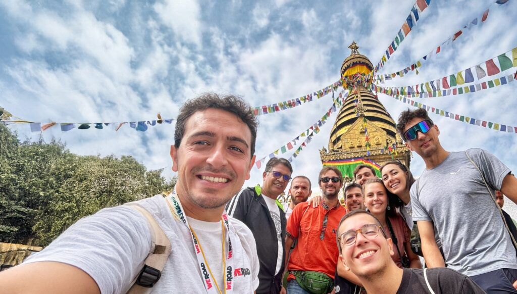 Ein Gruppen-Selfie von WeRoad-Reisenden vor dem Swayambhunath-Stupa in Kathmandu, umgeben von bunten Gebetsfahnen.