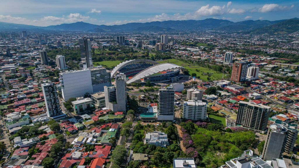Eine beeindruckende Luftaufnahme von San José, Costa Rica, die das moderne Nationalstadion und die Stadtlandschaft vor einer bergigen Kulisse zeigt.