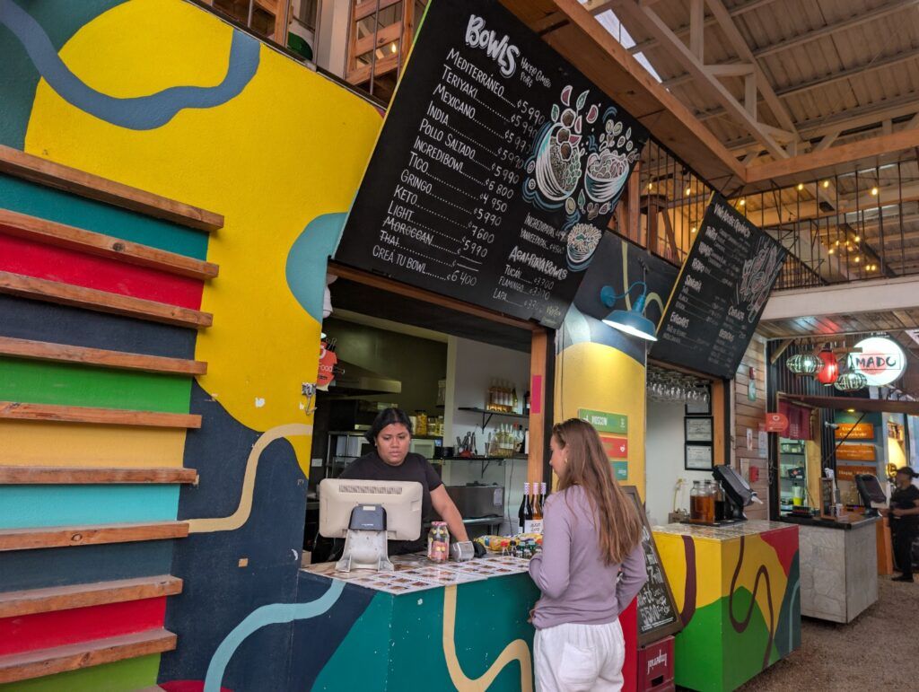 Eine moderne, farbenfrohe Essensbude mit einer großen Speisekarte für verschiedene 'Bowls' in einer Markthalle in Costa Rica.