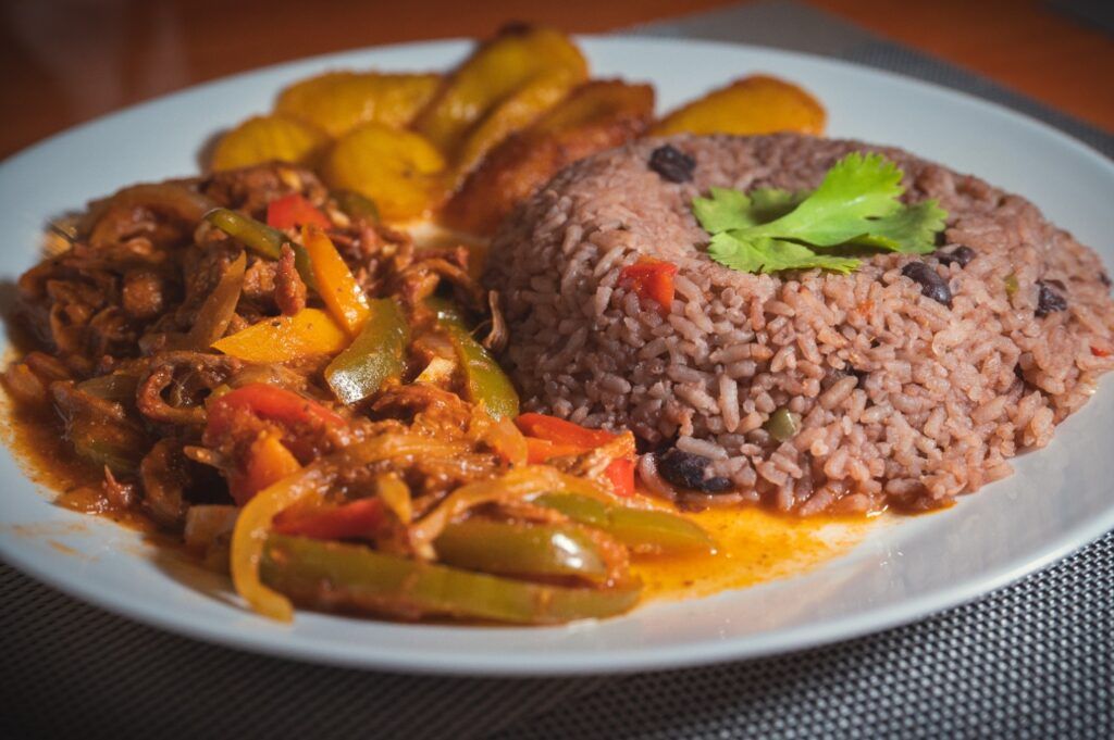 A traditional Cuban dish of Ropa Vieja served with Congri (rice and black beans) and fried plantains on a white plate.