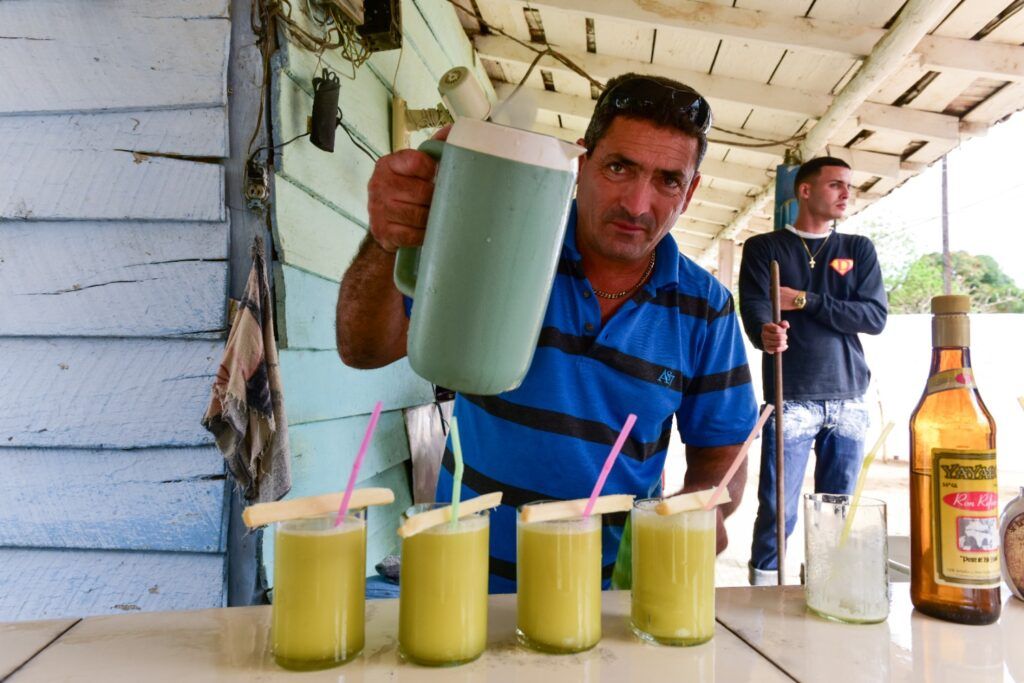 Un homme verse du guarapo frais dans des verres garnis de morceaux de canne à sucre sur un stand rustique à Cuba.