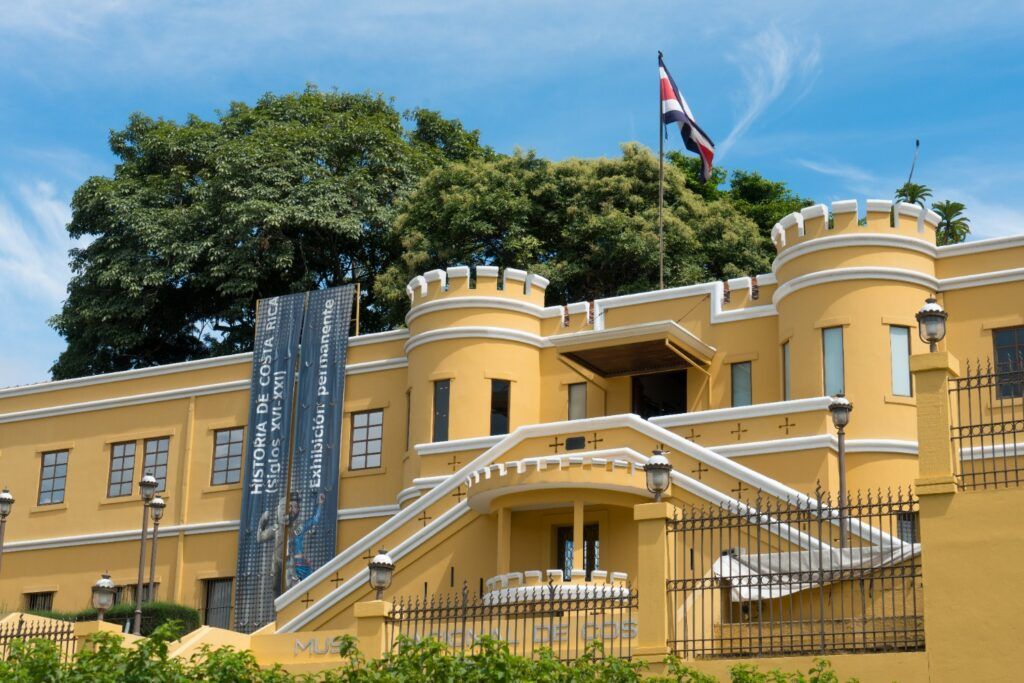 Das gelbe Nationalmuseum von Costa Rica in San José, ein ehemaliges Fort mit Zinnen und einer wehenden Nationalflagge unter blauem Himmel.