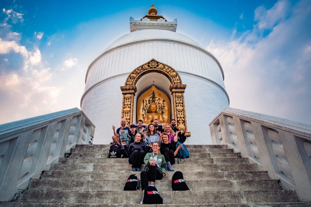 Eine Gruppe von WeRoad-Reisenden sitzt auf den Stufen der World Peace Pagoda in Pokhara, Nepal.